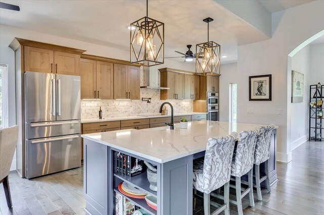 kitchen featuring light stone countertops, stainless steel appliances, sink, a center island with sink, and light hardwood / wood-style flooring