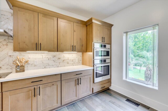 kitchen with double oven, light brown cabinetry, tasteful backsplash, and light wood-type flooring