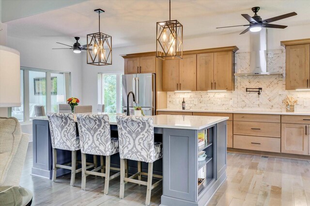 kitchen featuring decorative backsplash, stainless steel fridge, wall chimney exhaust hood, a breakfast bar, and an island with sink