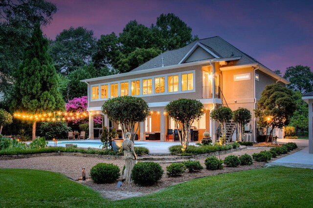 back house at dusk with a balcony and a patio area