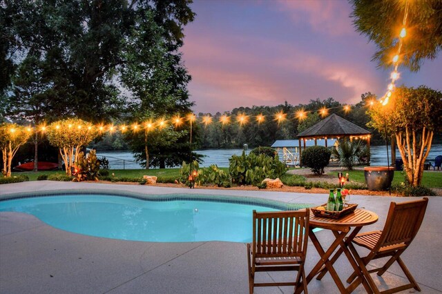 pool at dusk featuring a gazebo, a patio, and a water view