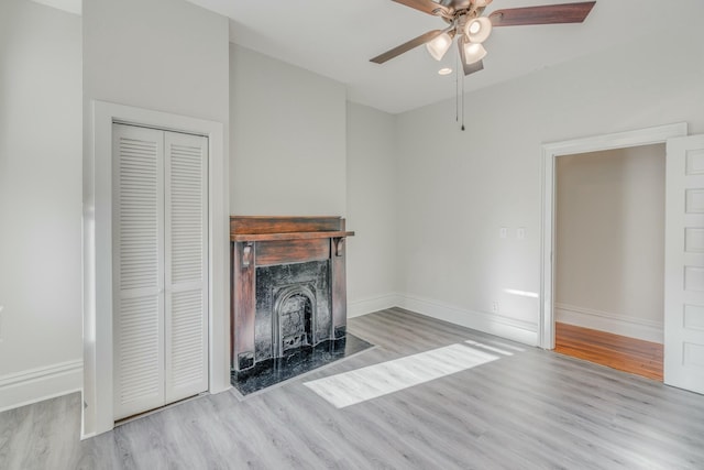 unfurnished living room with a premium fireplace, baseboards, a ceiling fan, and wood finished floors