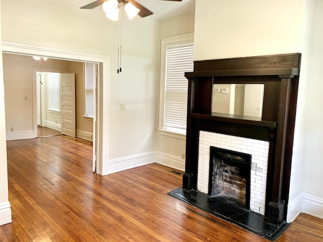 unfurnished living room with ceiling fan, a fireplace, visible vents, hardwood / wood-style floors, and baseboards