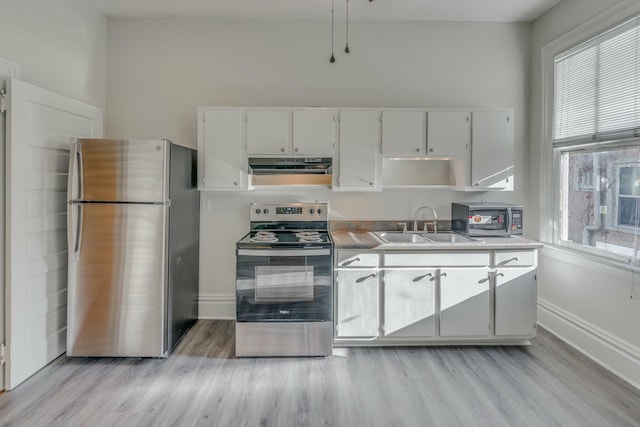 kitchen with a sink, a wealth of natural light, appliances with stainless steel finishes, light wood-style floors, and under cabinet range hood