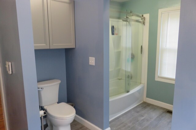 bathroom featuring wood-type flooring, toilet, and bath / shower combo with glass door