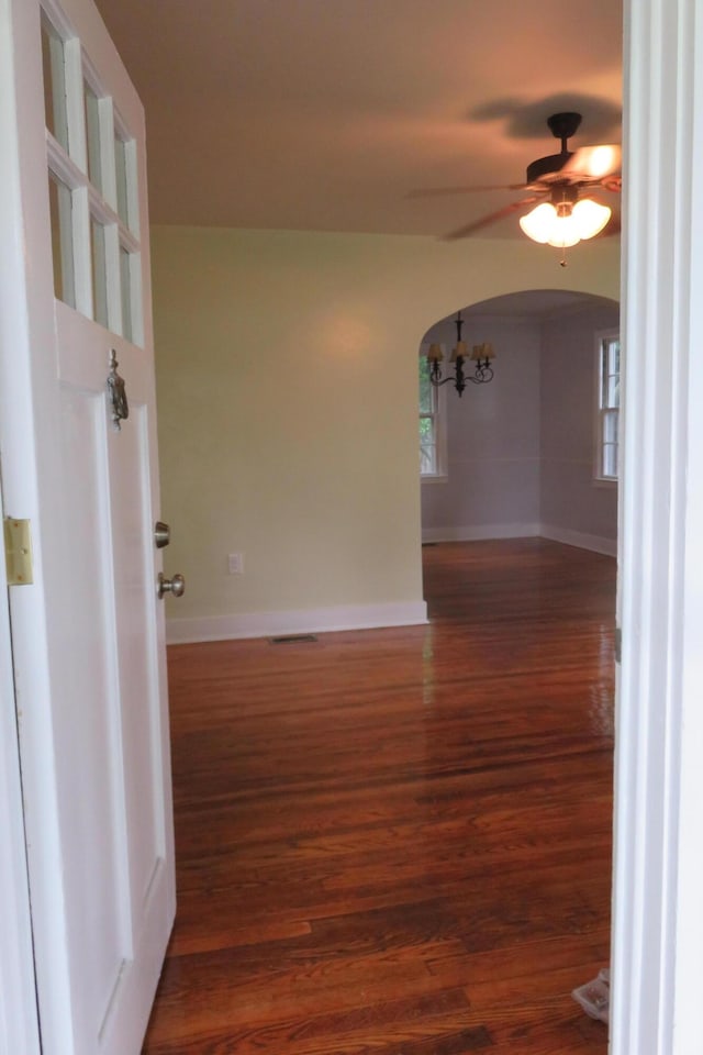 empty room with ceiling fan with notable chandelier, a healthy amount of sunlight, and dark hardwood / wood-style floors