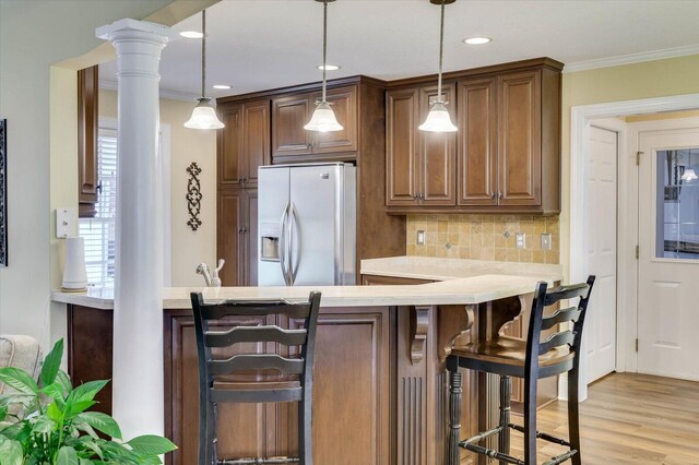 kitchen with stainless steel refrigerator with ice dispenser, backsplash, decorative columns, crown molding, and pendant lighting