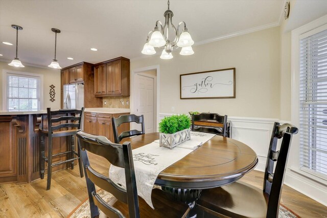 dining area with light hardwood / wood-style flooring, crown molding, and a notable chandelier