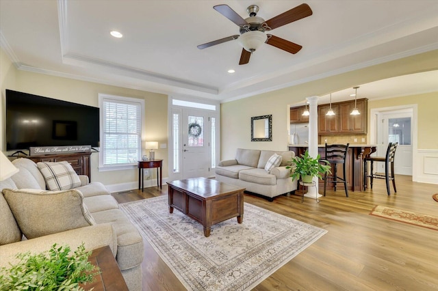 living room with light wood-type flooring, a raised ceiling, ceiling fan, and crown molding