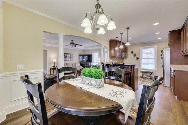 dining area featuring hardwood / wood-style floors, ceiling fan with notable chandelier, ornamental molding, and ornate columns