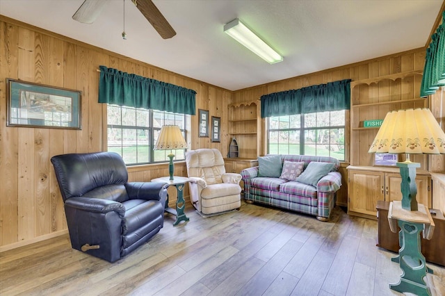 sitting room with built in shelves, ceiling fan, wooden walls, and light hardwood / wood-style floors