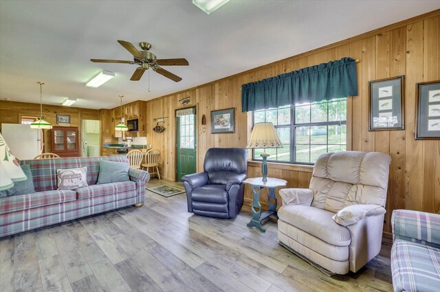 living room featuring ceiling fan, light hardwood / wood-style floors, and wood walls