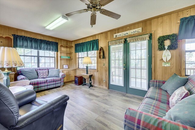 living room with ceiling fan, a healthy amount of sunlight, wooden walls, and light hardwood / wood-style flooring