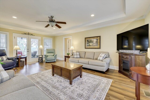 living room featuring ceiling fan, french doors, a raised ceiling, light wood-type flooring, and ornamental molding