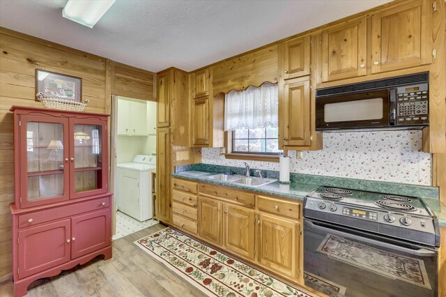 kitchen with washing machine and clothes dryer, sink, black appliances, and light hardwood / wood-style flooring