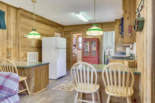 kitchen with white refrigerator, kitchen peninsula, hanging light fixtures, and wooden walls