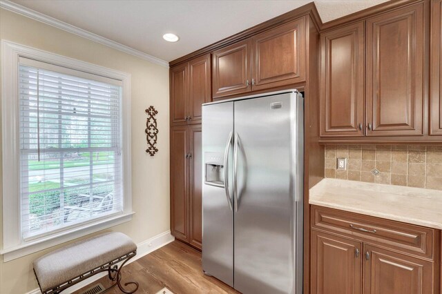 kitchen featuring decorative backsplash, stainless steel fridge, light wood-type flooring, and ornamental molding