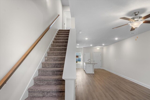 staircase featuring ceiling fan, sink, and hardwood / wood-style flooring