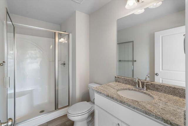 bathroom featuring a shower with door, vanity, and toilet