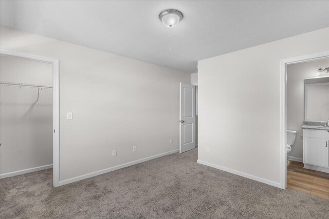 unfurnished bedroom with a walk in closet, light colored carpet, ensuite bath, and a closet