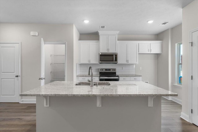 kitchen with light stone countertops, a center island with sink, stainless steel appliances, and sink