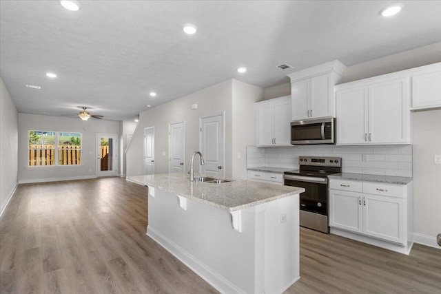 kitchen with white cabinets, appliances with stainless steel finishes, ceiling fan, and an island with sink