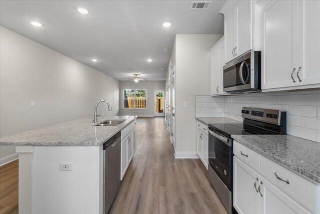 kitchen featuring light stone countertops, stainless steel appliances, sink, white cabinets, and an island with sink