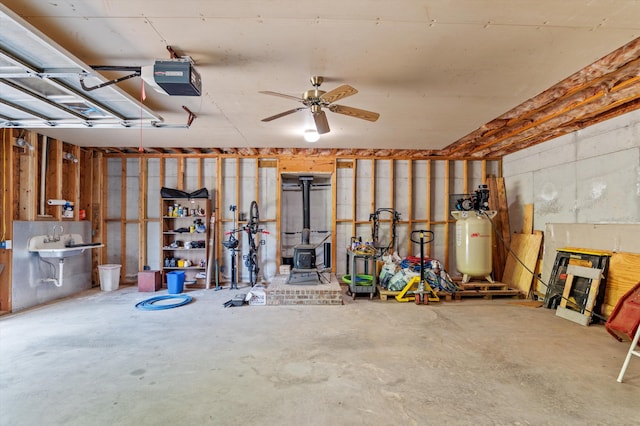 garage featuring a garage door opener, a wood stove, a ceiling fan, and a sink