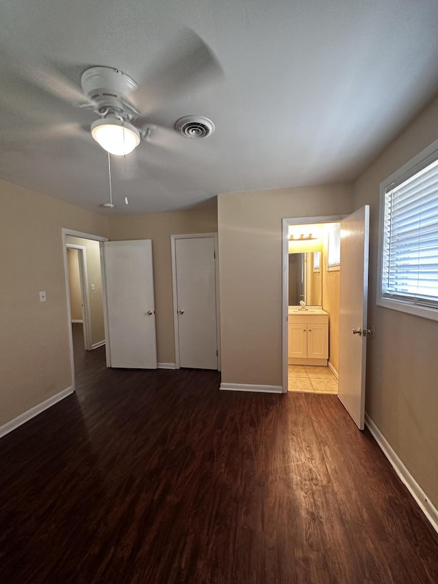 unfurnished bedroom featuring connected bathroom, ceiling fan, and dark wood-type flooring