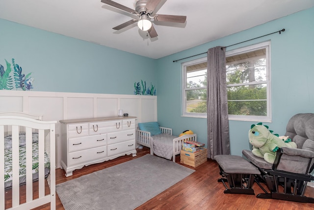 2211 Mura Dr, Augusta, GA 30906 - bedroom featuring wood finished floors, a decorative wall, a wainscoted wall, ceiling fan, and a nursery area
