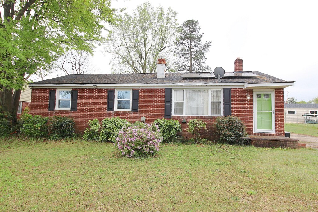 view of front of property with a chimney, brick siding, solar panels, and a front lawn