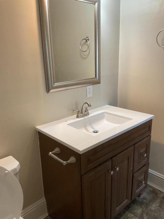 half bathroom with baseboards, toilet, and vanity