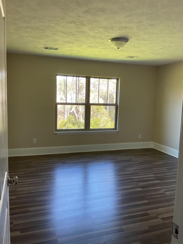 spare room with dark wood finished floors, visible vents, a textured ceiling, and baseboards