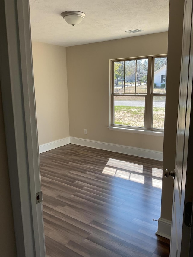 spare room featuring dark wood-type flooring, baseboards, visible vents, and a textured ceiling