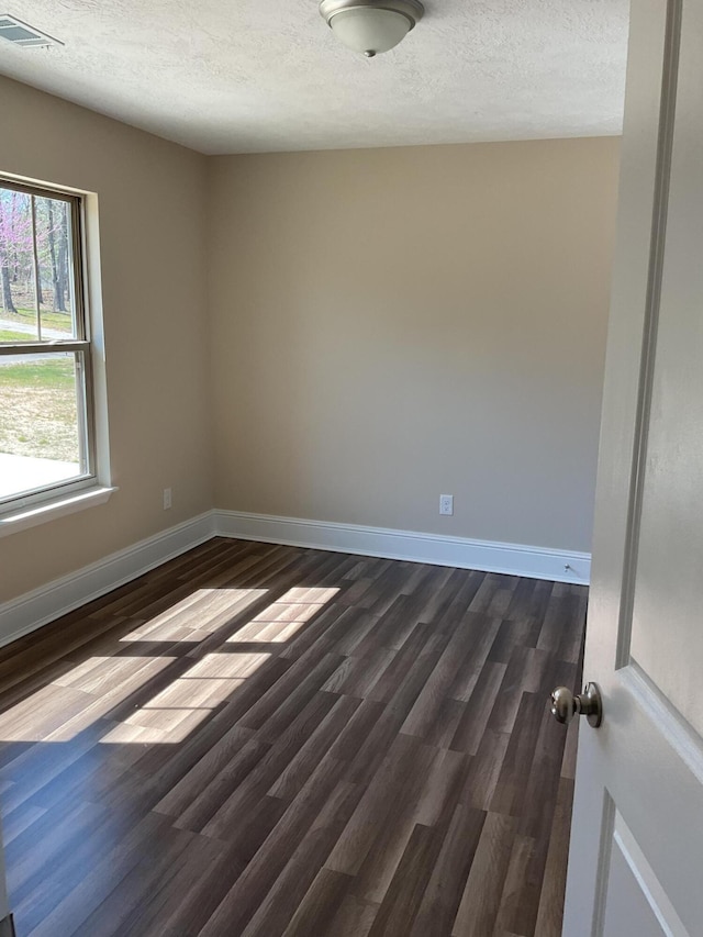 unfurnished room featuring dark wood finished floors, visible vents, a textured ceiling, and baseboards