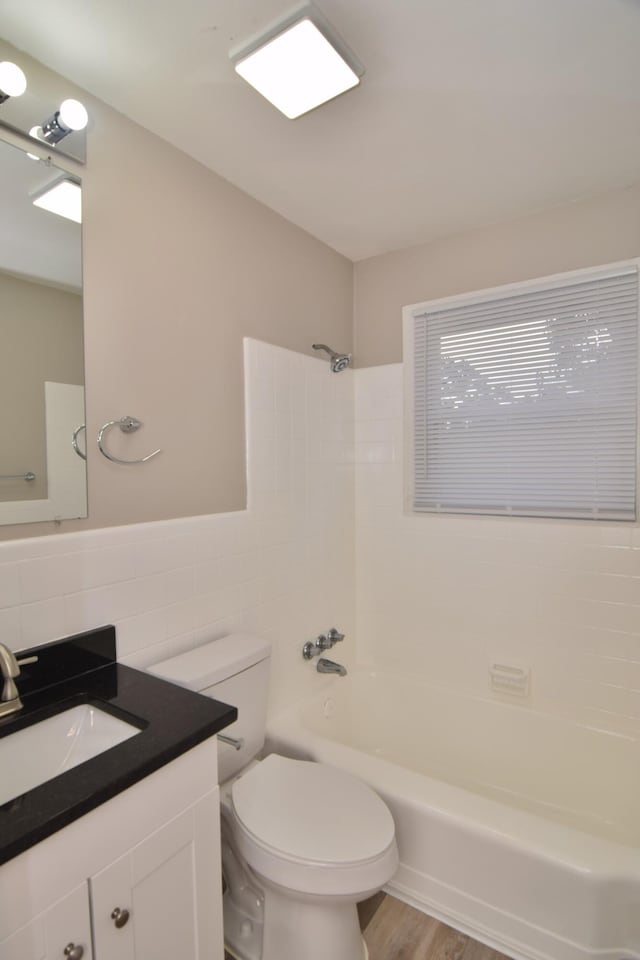 full bath featuring toilet, tile walls, shower / bathtub combination, wood finished floors, and vanity