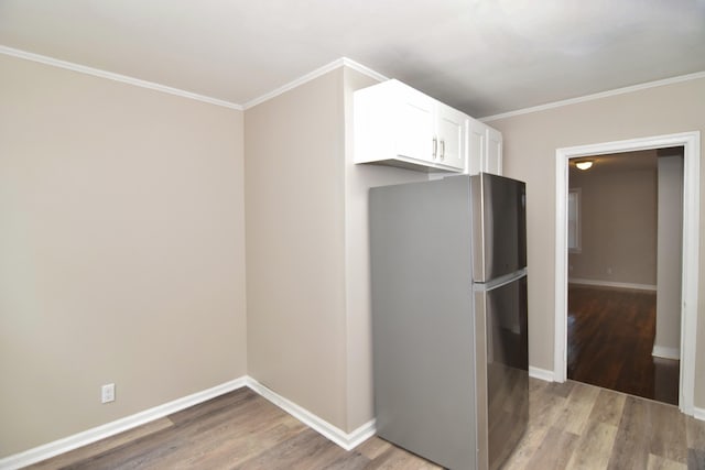 kitchen featuring crown molding, light wood-style floors, baseboards, white cabinetry, and freestanding refrigerator