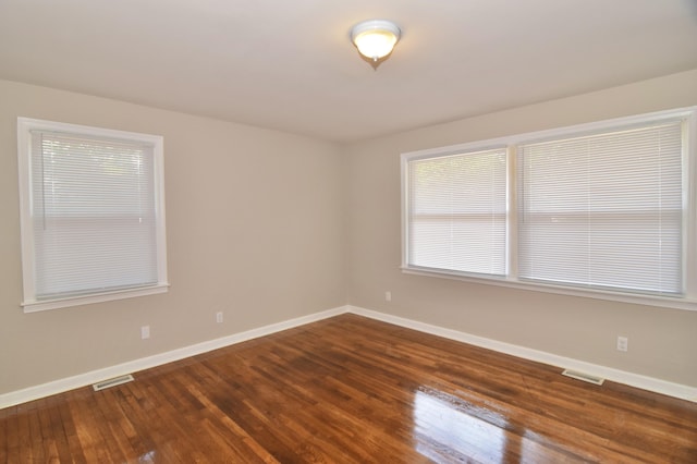 empty room with wood finished floors, visible vents, baseboards, and plenty of natural light