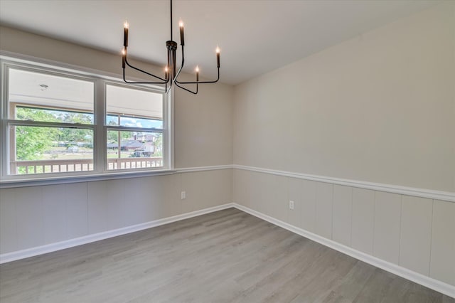 unfurnished room with an inviting chandelier, baseboards, and wood finished floors