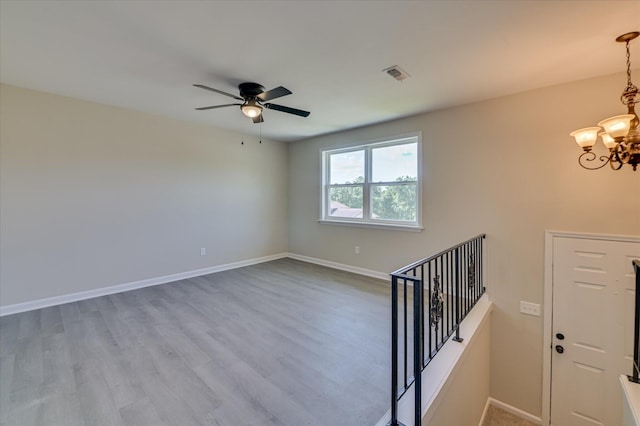 empty room with baseboards, ceiling fan with notable chandelier, wood finished floors, and visible vents
