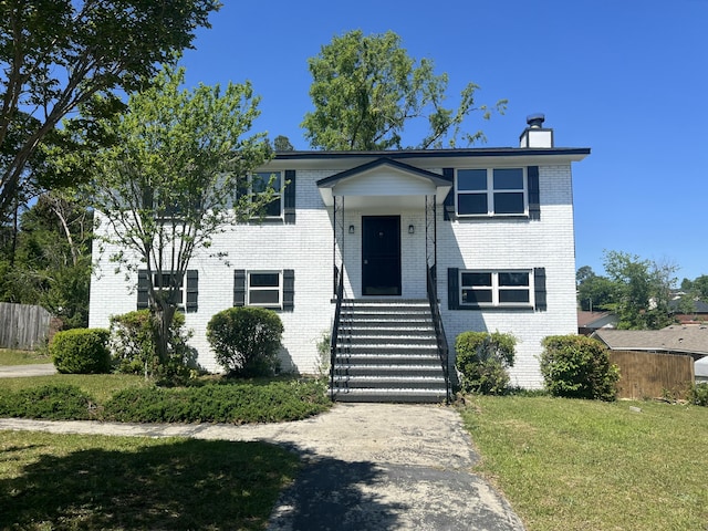 split foyer home featuring brick siding, fence, a chimney, and a front yard