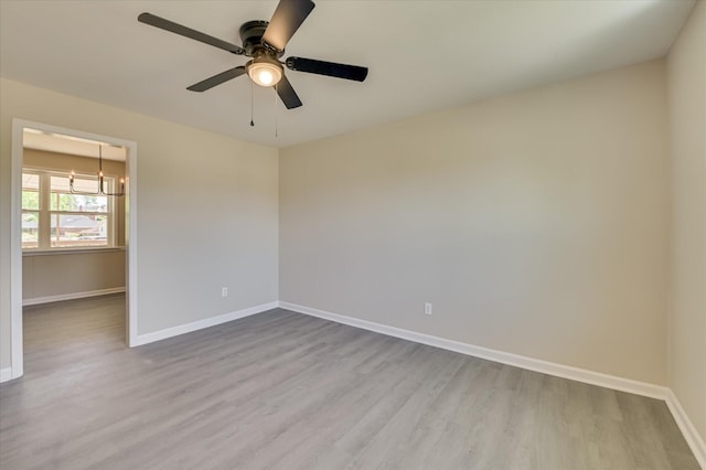 unfurnished room with baseboards, ceiling fan with notable chandelier, and wood finished floors