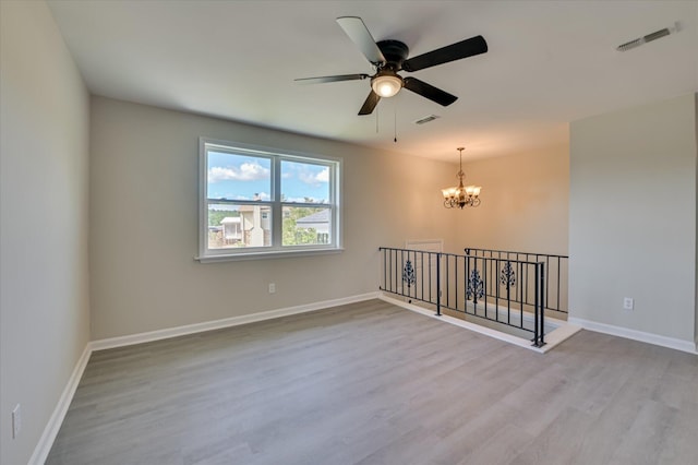 spare room featuring baseboards, ceiling fan with notable chandelier, wood finished floors, and visible vents