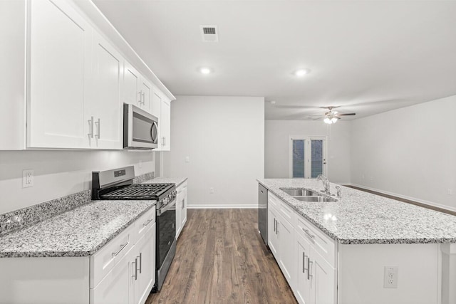 kitchen featuring appliances with stainless steel finishes, sink, white cabinetry, light stone counters, and an island with sink