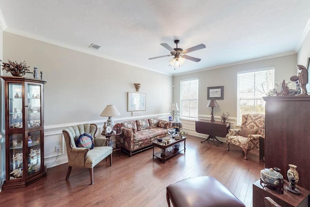 living room with visible vents, ornamental molding, wainscoting, ceiling fan, and wood finished floors