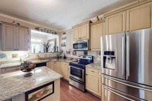 kitchen with light brown cabinetry, appliances with stainless steel finishes, dark wood-type flooring, and light stone countertops