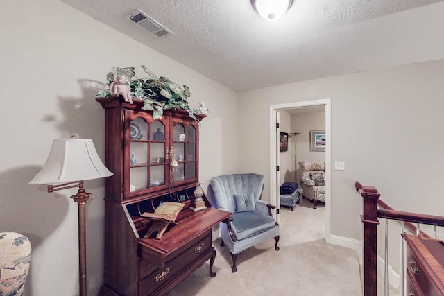 sitting room with light carpet, a textured ceiling, visible vents, and baseboards