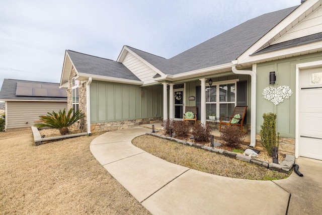 doorway to property featuring covered porch, stone siding, a shingled roof, and board and batten siding