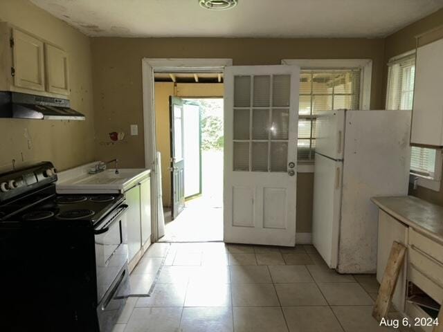 kitchen featuring black / electric stove, sink, light tile patterned floors, and white refrigerator