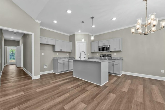 kitchen featuring dark wood-style flooring, an island with sink, appliances with stainless steel finishes, baseboards, and ornamental molding